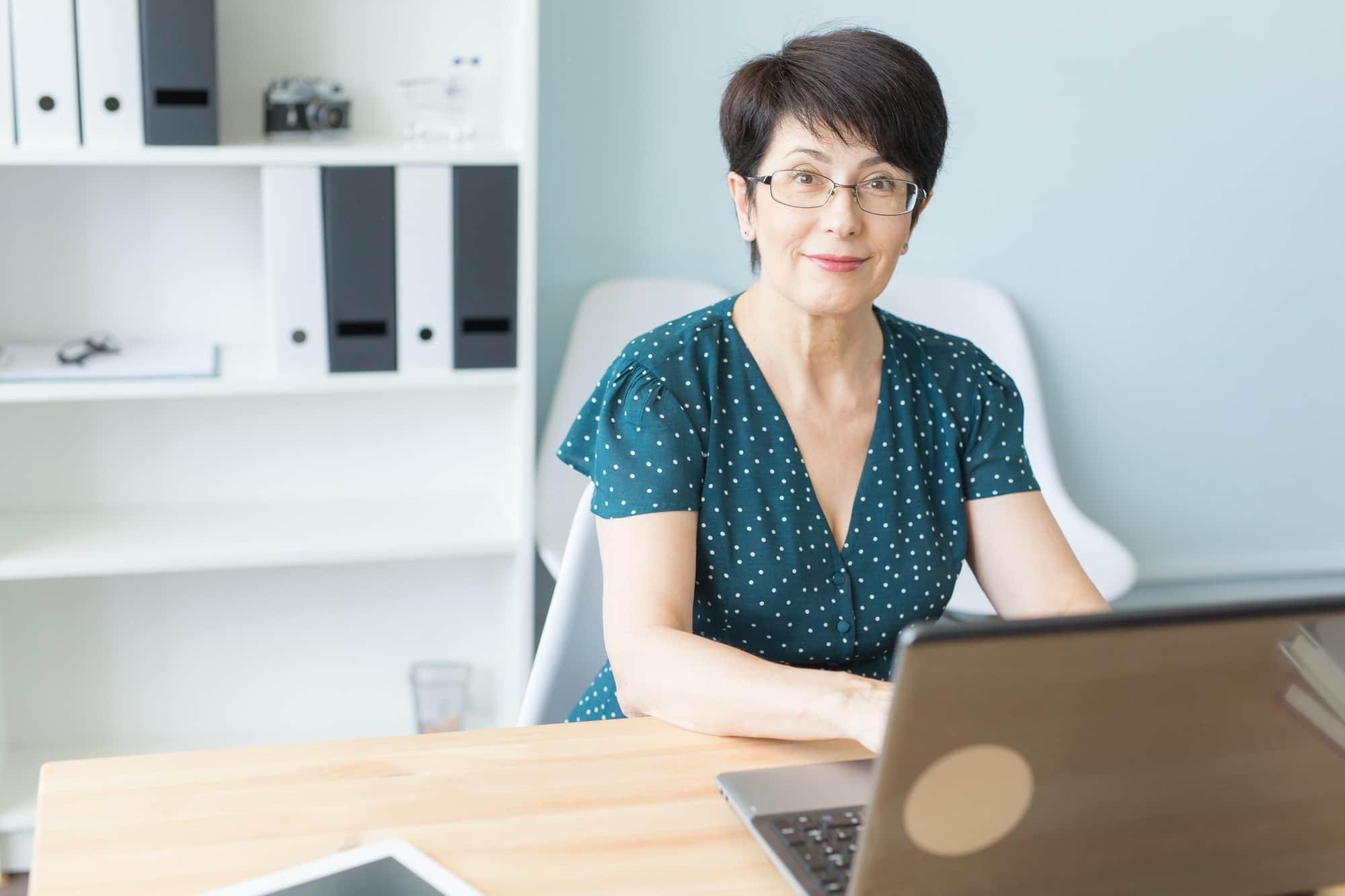 Business, technology and people concept - middle aged woman work in office and use a laptop