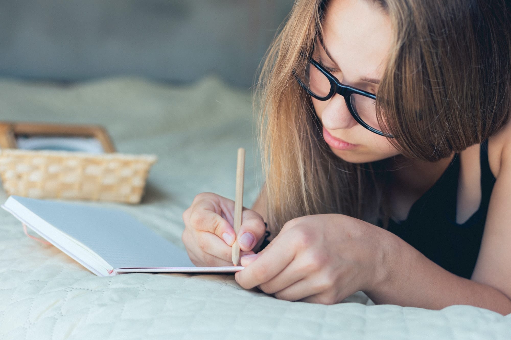 Satisfied and happy smiling girl lying on sofa in room, and writing notebook